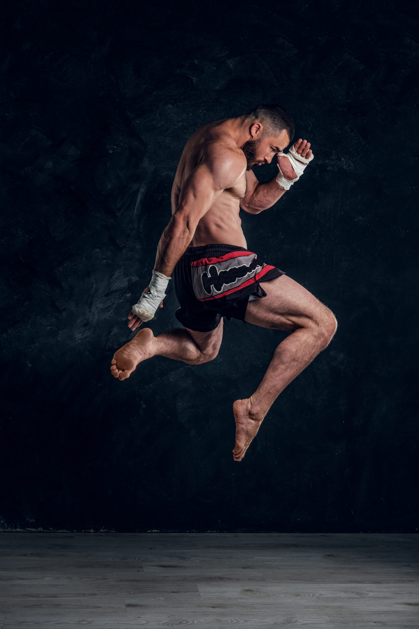 Focused physically fit man is jumping, making illusion of flight before punch an dark studio.